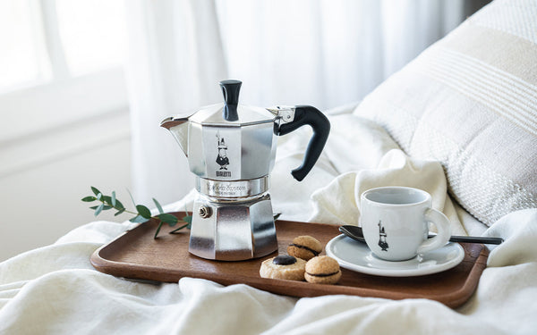 Classic Bialetti moka pot with a coffee cup on a wooden tray